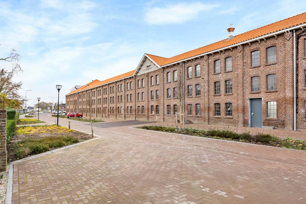 Buitenaanzicht van vergaderlocatie Onder de Pannen in Echt, een historisch pand met bakstenen gevel, grote industriële ramen en een oranje pannendak.